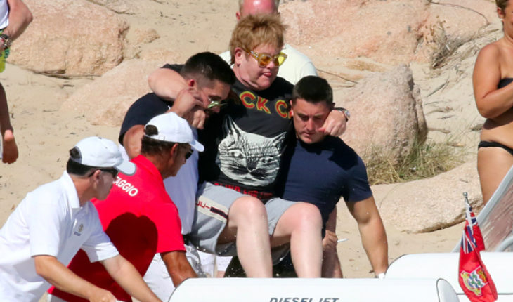 Elton John es llevado en brazos por sus guardias para no mojarse los pies