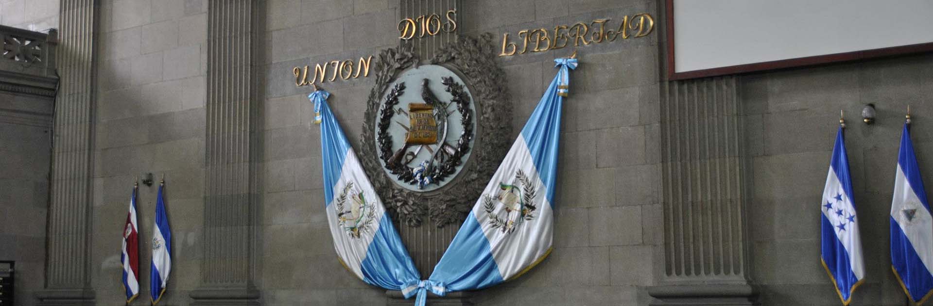 Detalle del podio presidencial del Congreso de Guatemala, con el escudo de la República, las banderas del país, y el lema "Dios, Unión y Libertad"